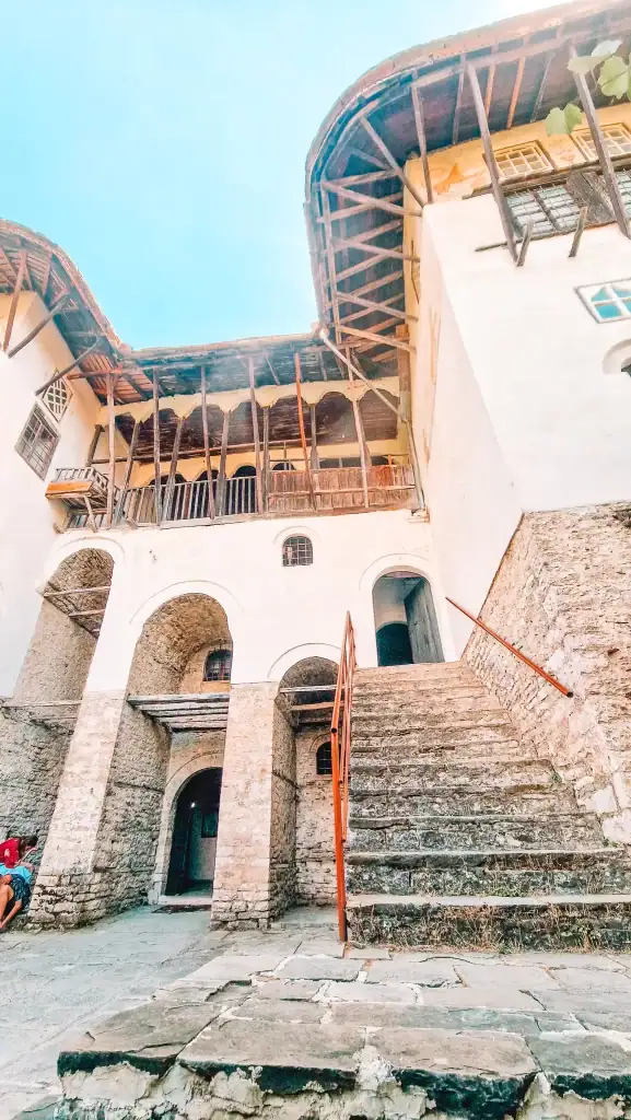 View from the stone courtyard of Skenduli House in Gjirokastër, showcasing Ottoman architecture with arched doorways and a timber-framed upper floor.