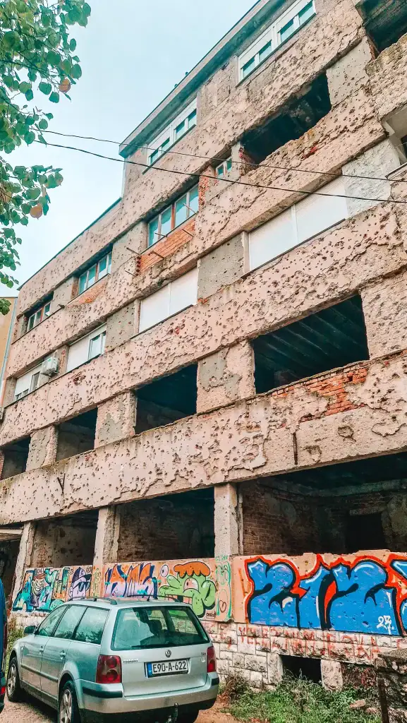 Close-up of a war-damaged building in Mostar, its concrete façade pocked with bullet holes and decorated with colorful graffiti. A haunting yet important landmark from the Bosnian War.