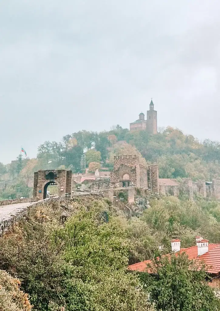 The Tsarevets Fortress in Veliko Tarnovo rising above the mist, with its stone walls and hilltop church surrounded by autumn trees.