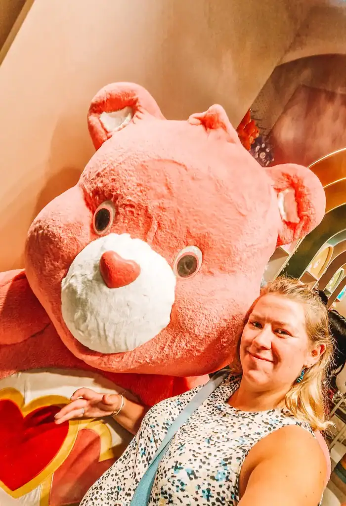 Em taking a selfie with a giant pink Care Bear inside a themed café, showcasing playful mall attractions in Bangkok.