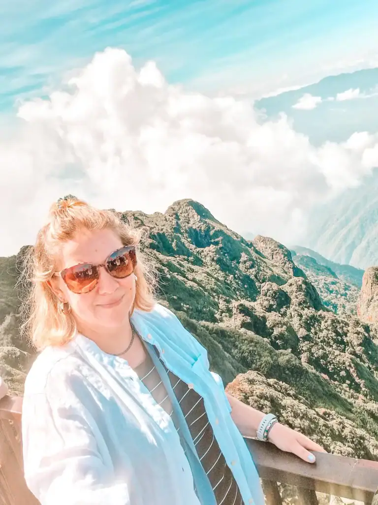 Em in sunglasses wearing a light jacket over a striped top while standing on a viewing platform above the clouds at Mount Fansipan in Sapa.