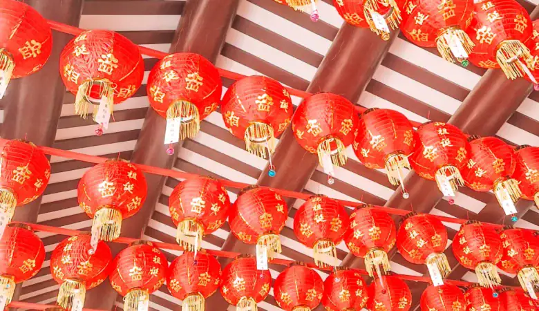Rows of vibrant red Chinese lanterns with golden characters hang from the ceiling of a temple in Singapore, creating a festive and traditional atmosphere.