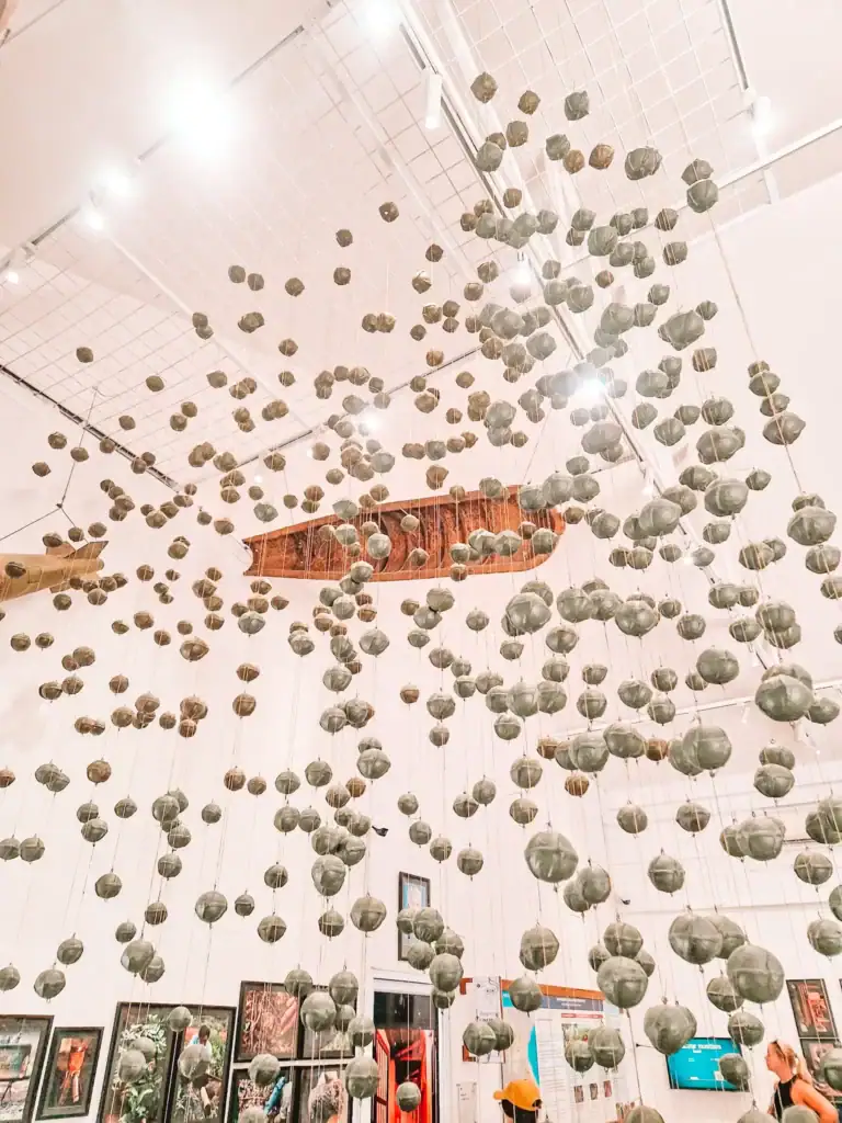 An art installation of suspended bombshell replicas hangs from the ceiling of a UXO museum, raising awareness about Laos’ war history with educational exhibits below.