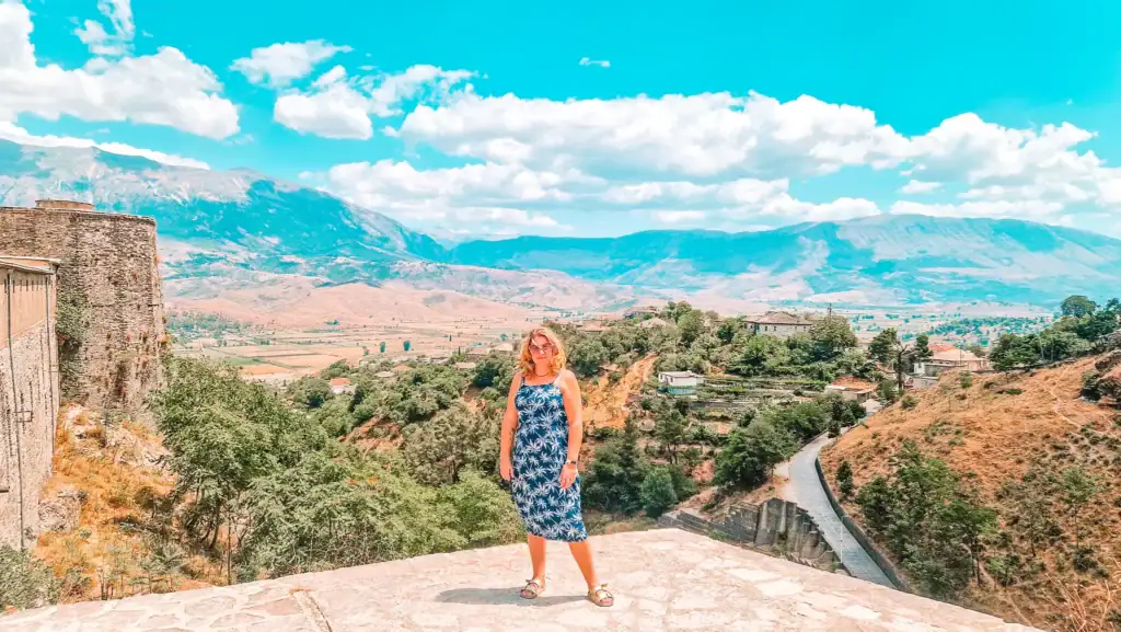 Em stands on a stone viewpoint above Gjirokastër with mountains and valley views stretching behind her. This shows the dramatic historic day trips available from Tirana.