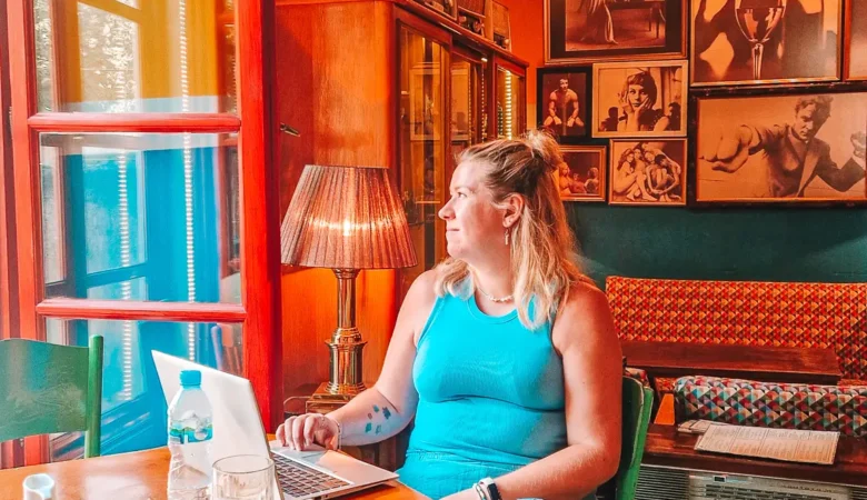 Em sits at a small wooden table working on a laptop inside a cosy vintage style café with warm orange walls, framed photos, and retro decor. This shows the relaxed and characterful café working experience you can expect when choosing between Skopje vs Tirana for digital nomads.